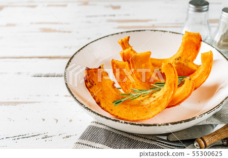 Slices of roasted pumpkin on white plate and white wooden background 55300625
