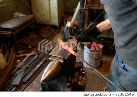 Blacksmith forging red-hot metal with hammer. 55301549