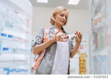Attentive blonde aged woman looking at vitamins 55307051
