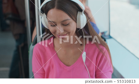 Young woman passenger enjoying trip at the public transport, sitting with headphones near the window Young woman passenger enjoying trip at the public transport, sitting with headphones near the window 55310813