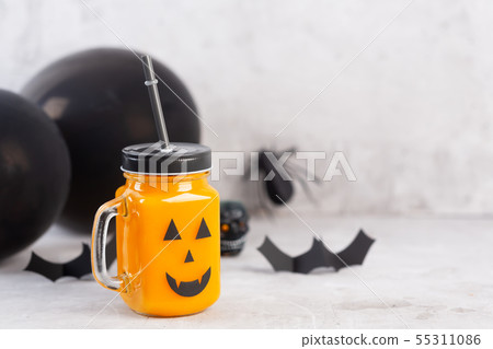 Halloween healthy pumpkin or carrot drink in the glass jar with scary face on a gray background Halloween healthy pumpkin or carrot drink in the glass jar with scary face on a gray background 55311086