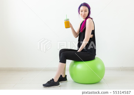 Cute young mixed race hipster girl with colored hair sitting on a green fitball and holding a banana 55314587