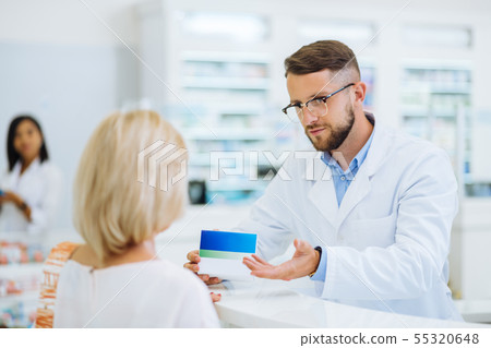 Attentive bearded chemist demonstrating package with pills Attentive bearded chemist demonstrating package with pills 55320648