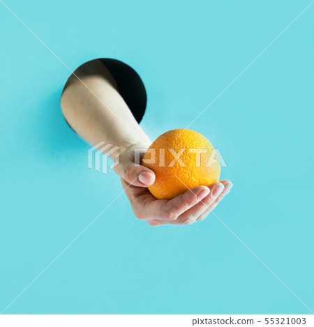 Female hand holding ripe orange in paper hole. Female hand holding ripe orange in paper hole. 55321003