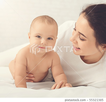 Adorable baby trying to crawl along white bed 55321385