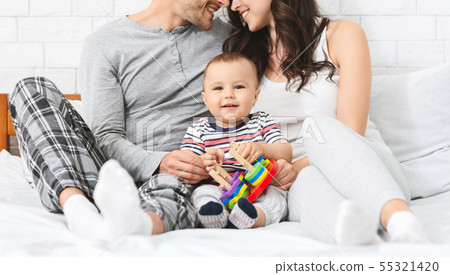 Sweet little baby smiling, sitting on bed with loving parents Sweet little baby smiling, sitting on bed with loving parents 55321420