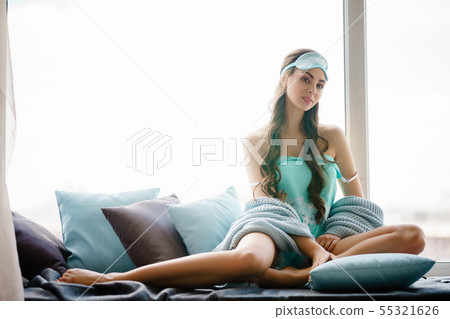 Beautiful young woman seating at window pillows in 55321626