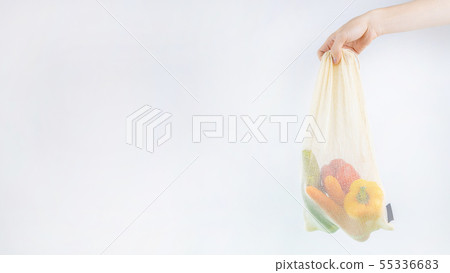 Hand holding net bag with vegetables inside. Hand holding net bag with vegetables inside. 55336683