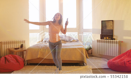 Happy carefree young brunette woman dancing alone in headphones in room with big window listen to 55342158