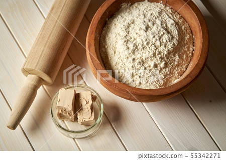 Top view of bowl of flour with yeast and rolling pin on  white  kitchen table 55342271