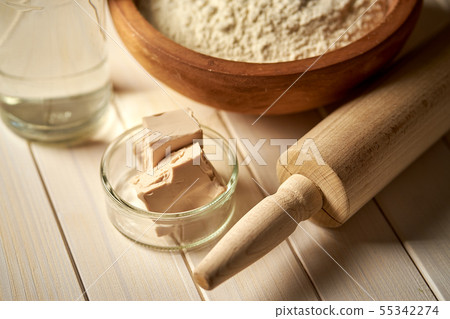 Top view of bowl of flour with yeast and rolling pin on white kitchen table Top view of bowl of flour with yeast and rolling pin on white kitchen table 55342274
