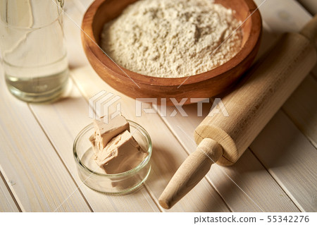 Top view of bowl of flour with yeast and rolling pin on white kitchen table Top view of bowl of flour with yeast and rolling pin on white kitchen table 55342276