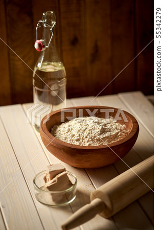 Top view of bowl of flour with yeast and rolling pin on white kitchen table Top view of bowl of flour with yeast and rolling pin on white kitchen table 55342279