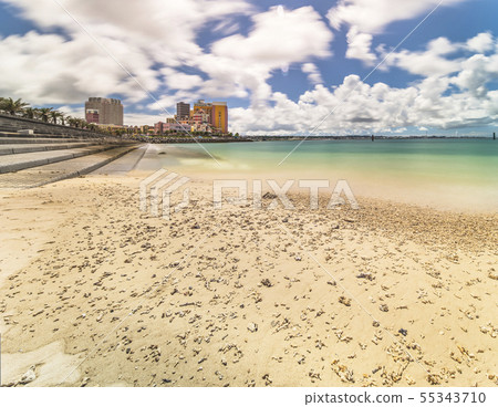 A palm-lined beach near an American village in Okinawa, a building standing in the background with a cobblestone A palm-lined beach near an American village in Okinawa, a building standing in the background with a cobblestone 55343710