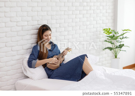 woman playing Ukulele on bed in cozy bedroom 55347891
