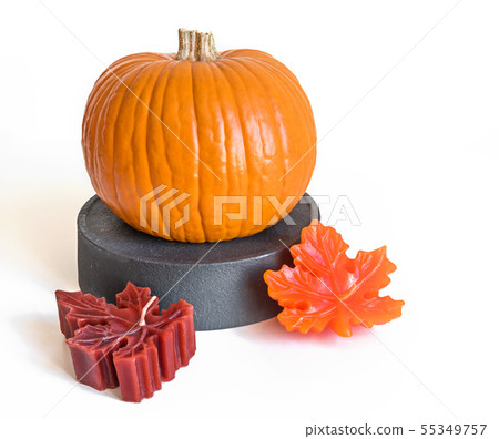 Small orange pumpkin on a gray stand and candle maple leaves isolated on white background Small orange pumpkin on a gray stand and candle maple leaves isolated on white background 55349757