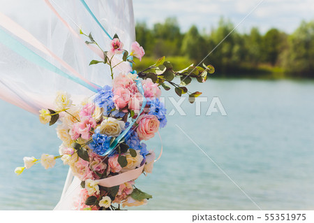 Part of the wedding arch decorated with fresh flowers is set on the sandy bank of the river. Wedding 55351975