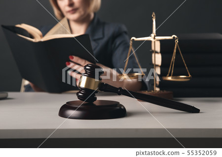 Woman lawyer reading professional books in office. Wooden gavel and libra on the desk. 55352059
