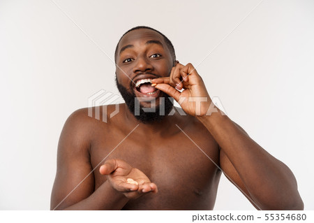 Sick African American guy eating medicine pill. Black man standing on plain background with copy 55354680