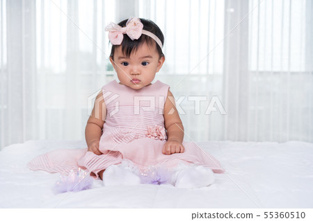 baby in pink dress on bed 55360510