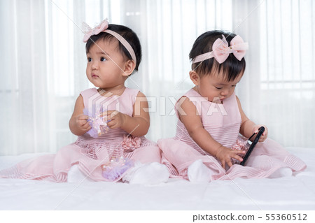 two twin babies in pink dress on bed, one playing two twin babies in pink dress on bed, one playing 55360512