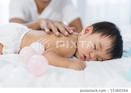 baby sleeping on bed with hand patting 55360564