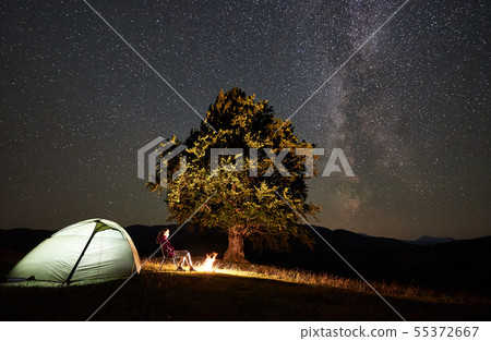 Woman resting at night camping in mountains under starry sky 55372667