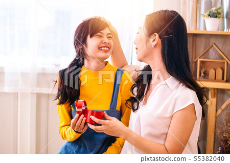 Asian middle-aged mother touching Smiling happy Asian teenage daughter in indoor living room at home 55382040
