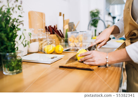 Female hands cutting lemon in a bright minimalistic kitchen. Female hands cutting lemon in a bright minimalistic kitchen. 55382341