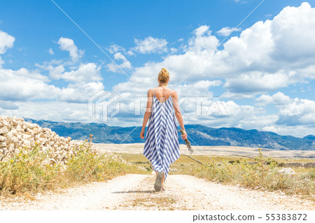 Rear view of woman in summer dress holding bouquet of lavender flowers while walking outdoor through 55383872
