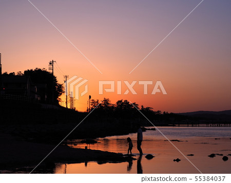 Silhouette of parent and child playing on the rainy sea coast at sunset 55384037