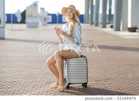 Happy woman sitting on suitcase and waiting taxi at airport Happy woman sitting on suitcase and waiting taxi at airport 55384979