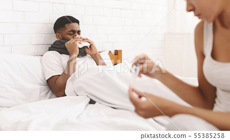 Woman taking care of sick man with fever lying in bed 55385258