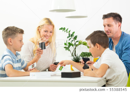 Happy young family playing card game at dining table at bright modern home. Happy young family playing card game at dining table at bright modern home. 55388545