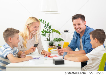 Happy young family playing card game at dining table at bright modern home. Happy young family playing card game at dining table at bright modern home. 55388548