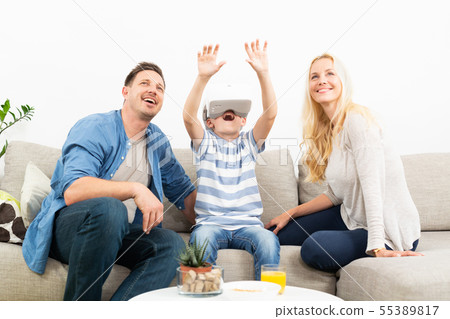 Happy family at home on living room sofa having fun playing games using virtual reality headset Happy family at home on living room sofa having fun playing games using virtual reality headset 55389817