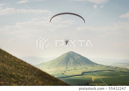 A paraglider flies in the sky in a cocoon suit on a paraglider above the mountain on a sunny summer A paraglider flies in the sky in a cocoon suit on a paraglider above the mountain on a sunny summer 55412247