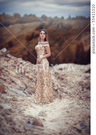 Girl in a golden dress on a background of rocks Girl in a golden dress on a background of rocks 55415310