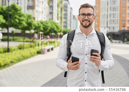 Man with backpack holding phone and black coffee cup. 55416786