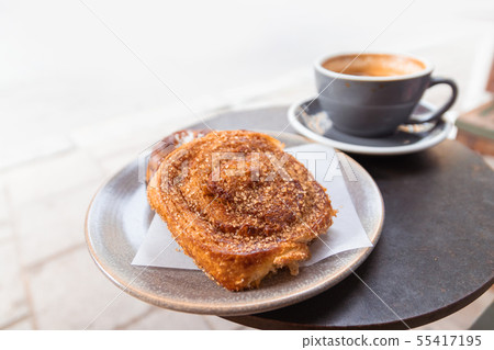Warm cinnamon bun with icing sugar with cup of Warm cinnamon bun with icing sugar with cup of 55417195