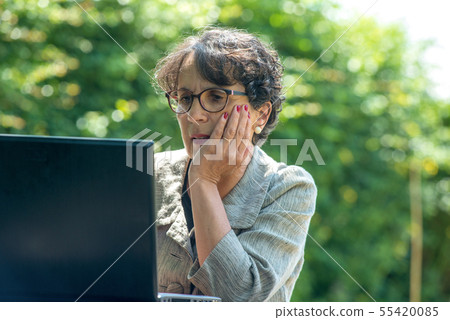 mature brunette using laptop in the garden mature brunette using laptop in the garden 55420085