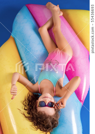 Beautiful little girl in colorful swimsuit and sunglasses lies , relax on an air mattress Beautiful little girl in colorful swimsuit and sunglasses lies , relax on an air mattress 55436693