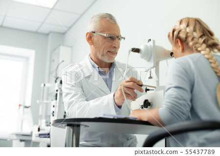 Grey-haired aged eye doctor wearing glasses consulting girl Grey-haired aged eye doctor wearing glasses consulting girl 55437789