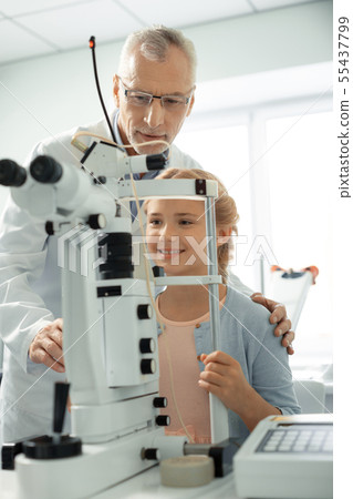 Grey-haired eye doctor wearing glasses standing near girl Grey-haired eye doctor wearing glasses standing near girl 55437799