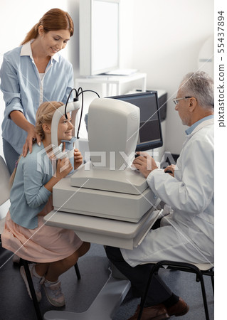Mommy touching shoulders of daughter having eye sight examination 55437894