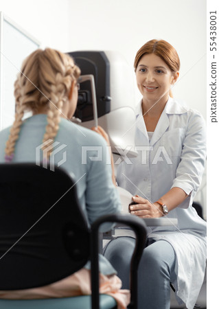 Eye specialist speaking to girl while examining eye sight 55438001