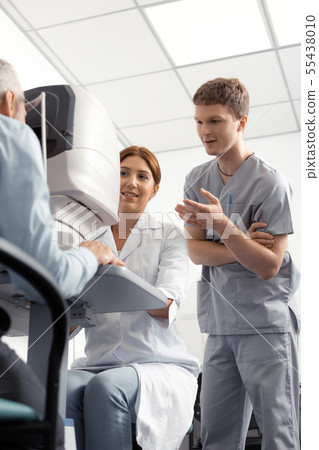 Dark-haired assistant standing near eye doctor during examination Dark-haired assistant standing near eye doctor during examination 55438010