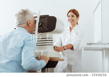 Red-haired eye doctor smiling while analyzing eye sight of patient Red-haired eye doctor smiling while analyzing eye sight of patient 55438258