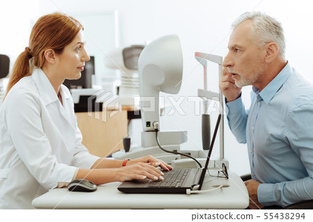 Eye specialist smiling while examining aged grey-haired man 55438294