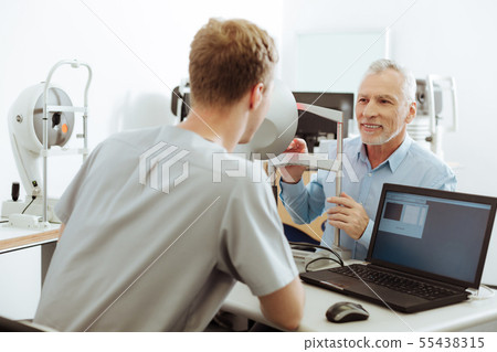 Female eye specialist sitting near laptop talking to her patient Female eye specialist sitting near laptop talking to her patient 55438315